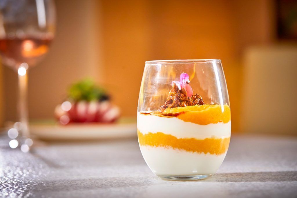 Un primer plano de un postre en una copa sobre una mesa con una copa de vino en el fondo.