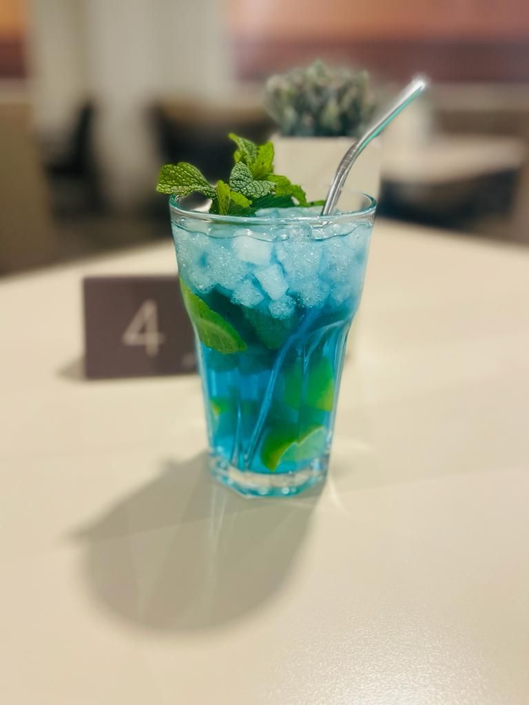 Una bebida azul con hielo y hojas de menta en un vaso sobre una mesa.