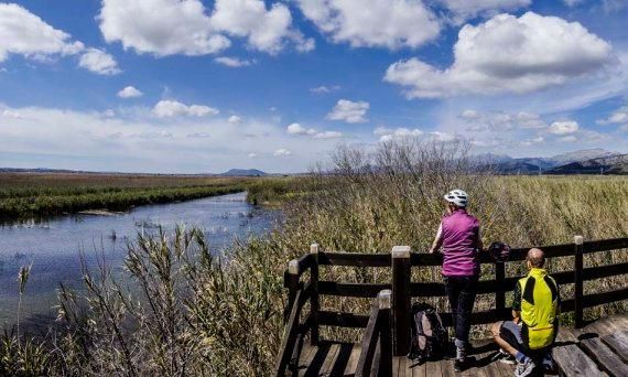 Dos personas están paradas en un puente de madera con vistas a un río.
