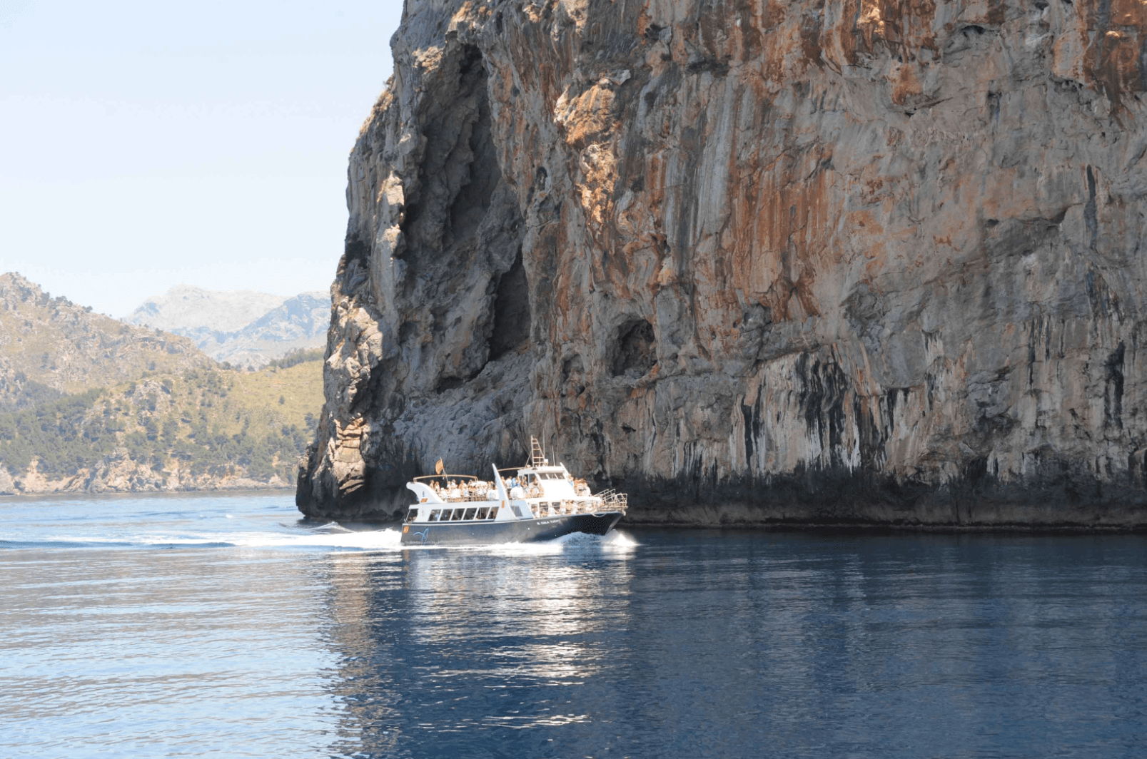 Un barco flota en el agua cerca de un acantilado rocoso.