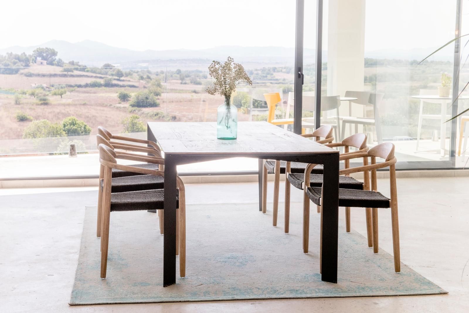 Una mesa de comedor con sillas y un jarrón con flores sobre ella.