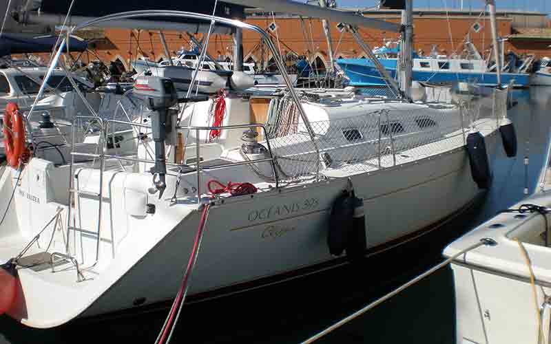 Un velero blanco está atracado en un puerto deportivo con otros barcos.