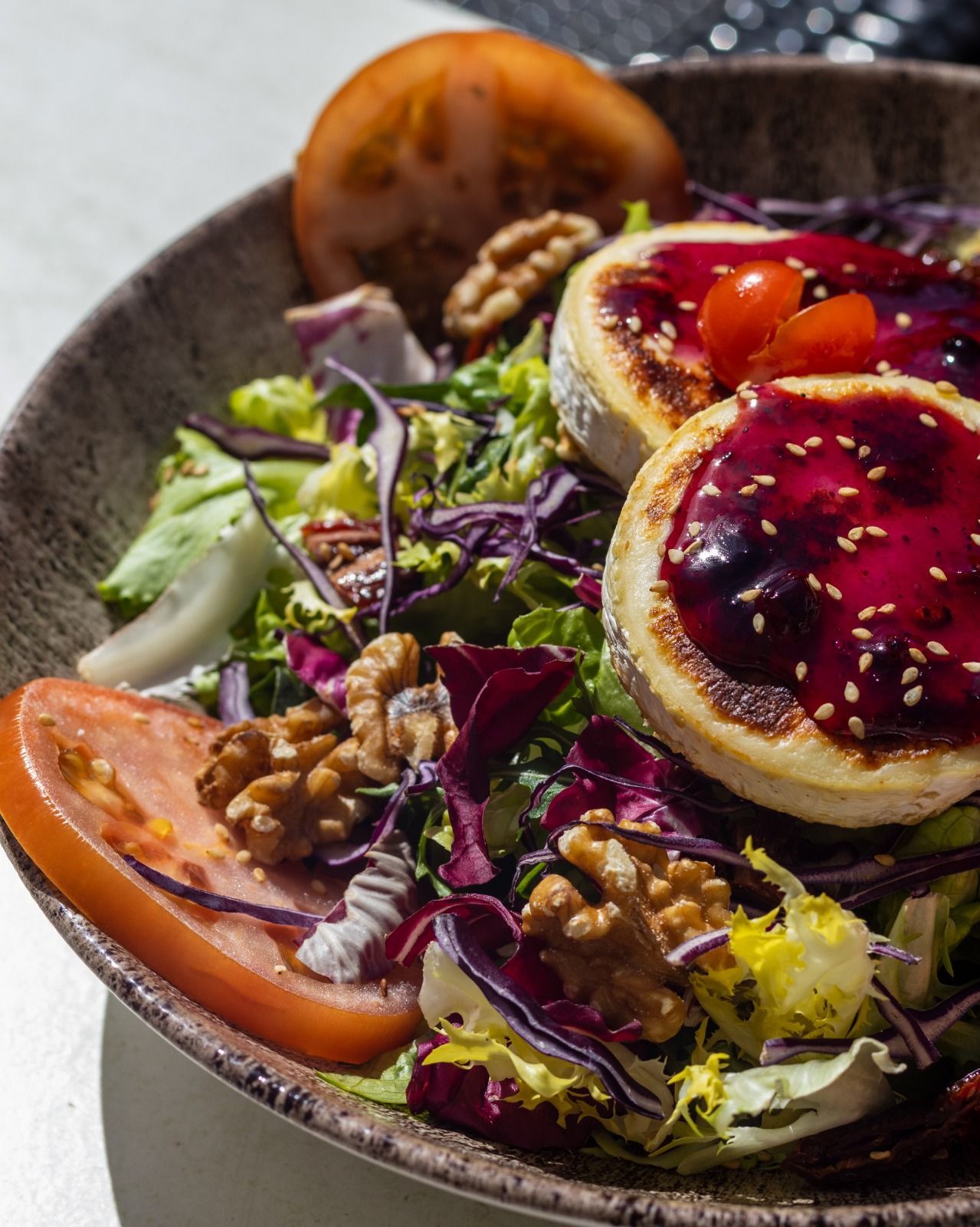 Una ensalada con queso de cabra, tomates, nueces y lechuga en un bol.