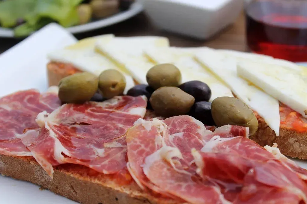 Un primer plano de un sándwich con jamón, aceitunas y queso.