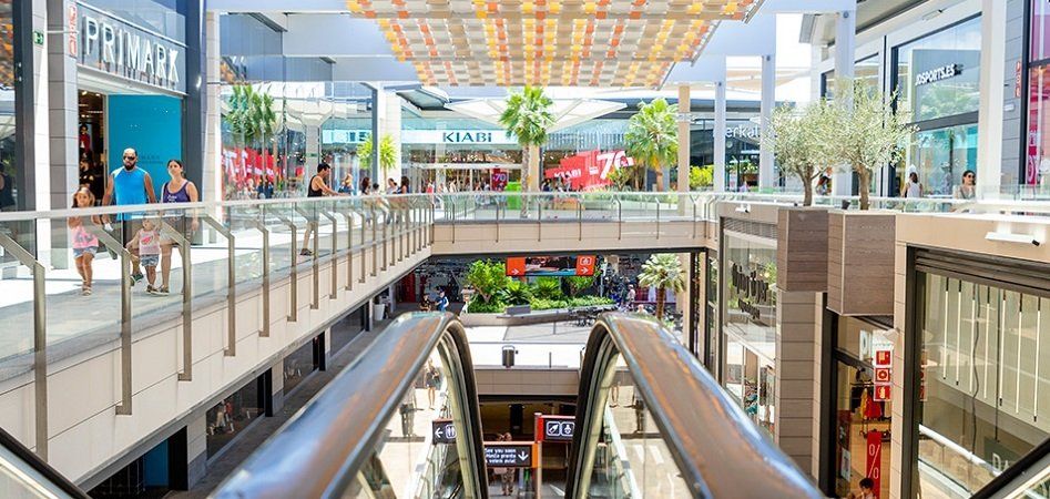 Un gran centro comercial con escaleras mecánicas y gente caminando.
