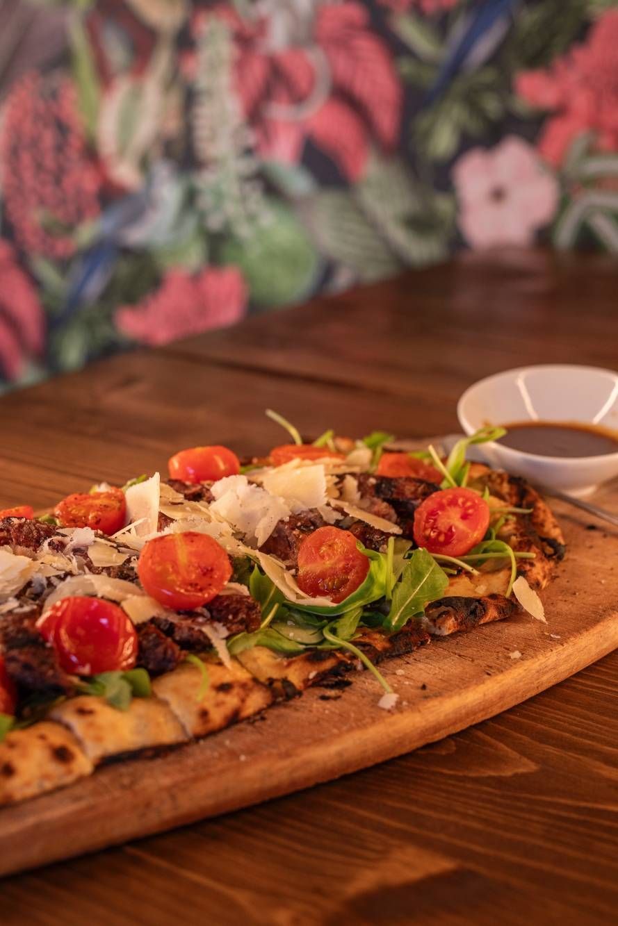 Una pizza con tomates y queso sobre una tabla de cortar de madera.