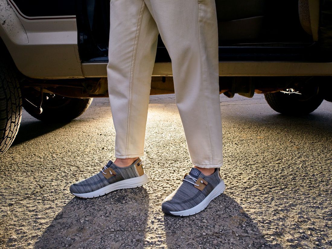 Una persona que lleva un par de zapatos está parada al lado de un coche.