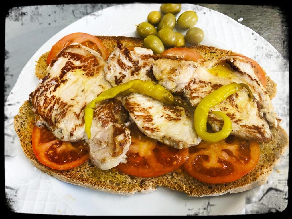Un sándwich con pollo, tomates, pimientos y aceitunas en un plato blanco.