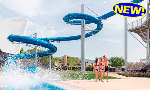 Un hombre y una mujer caminan frente a un tobogán de agua en un parque acuático.