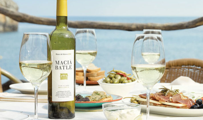 Una botella de vino blanco está sobre una mesa al lado de copas de vino.