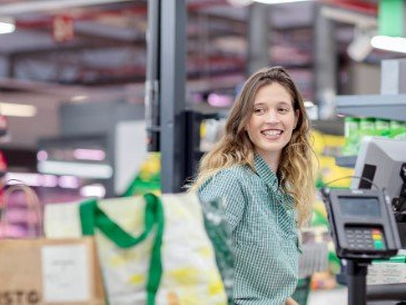 Una mujer sonríe mientras está parada en la caja registradora de una tienda de comestibles.
