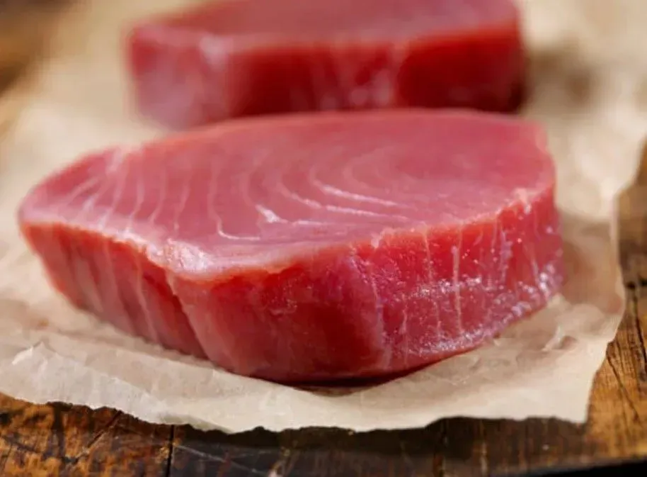 Dos filetes de atún crudo están sobre un trozo de papel sobre una mesa de madera.