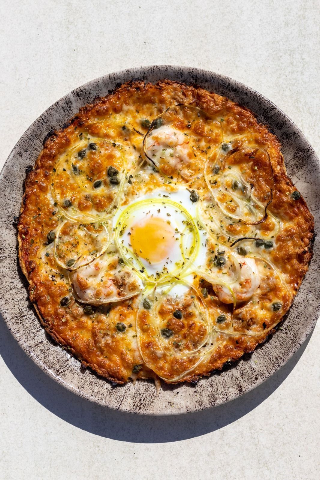 Una pizza con camarones y un huevo encima está en un plato.