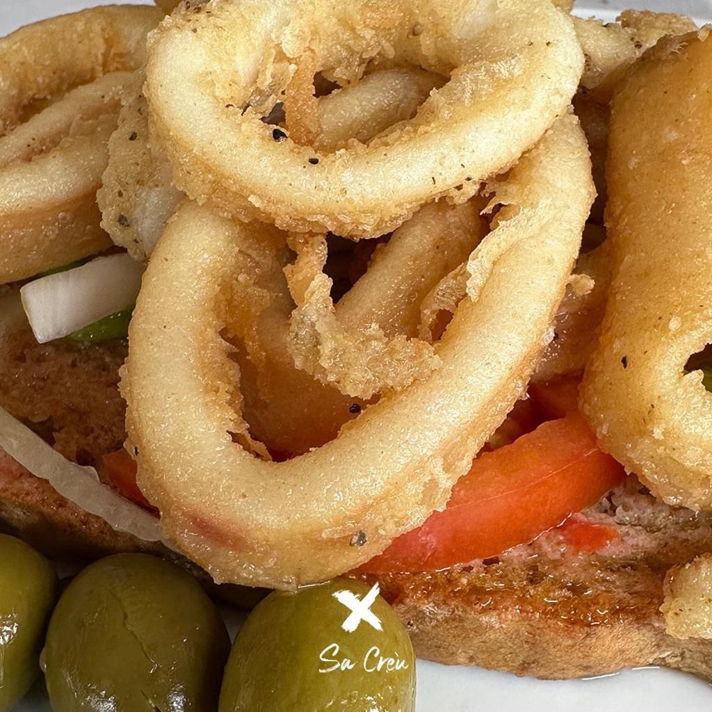 Un primer plano de un sándwich con aros de cebolla y tomates.