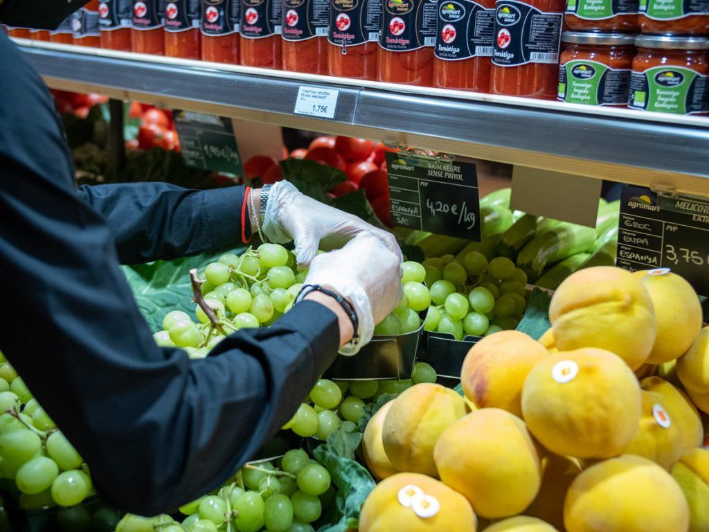 Una persona con guantes está recogiendo uvas en una tienda de comestibles.