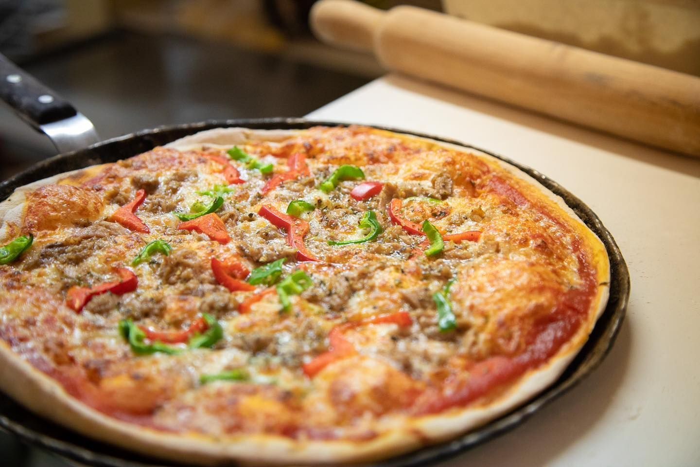 Una pizza reposa sobre una sartén sobre una mesa al lado de un rodillo.