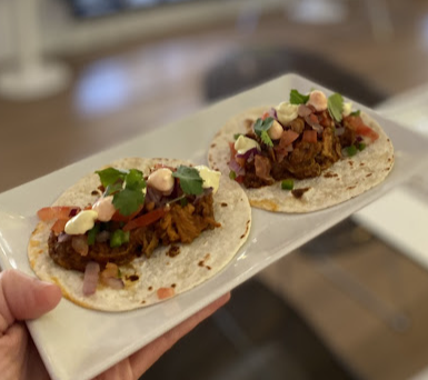 Una persona sostiene un plato blanco con dos tacos encima.