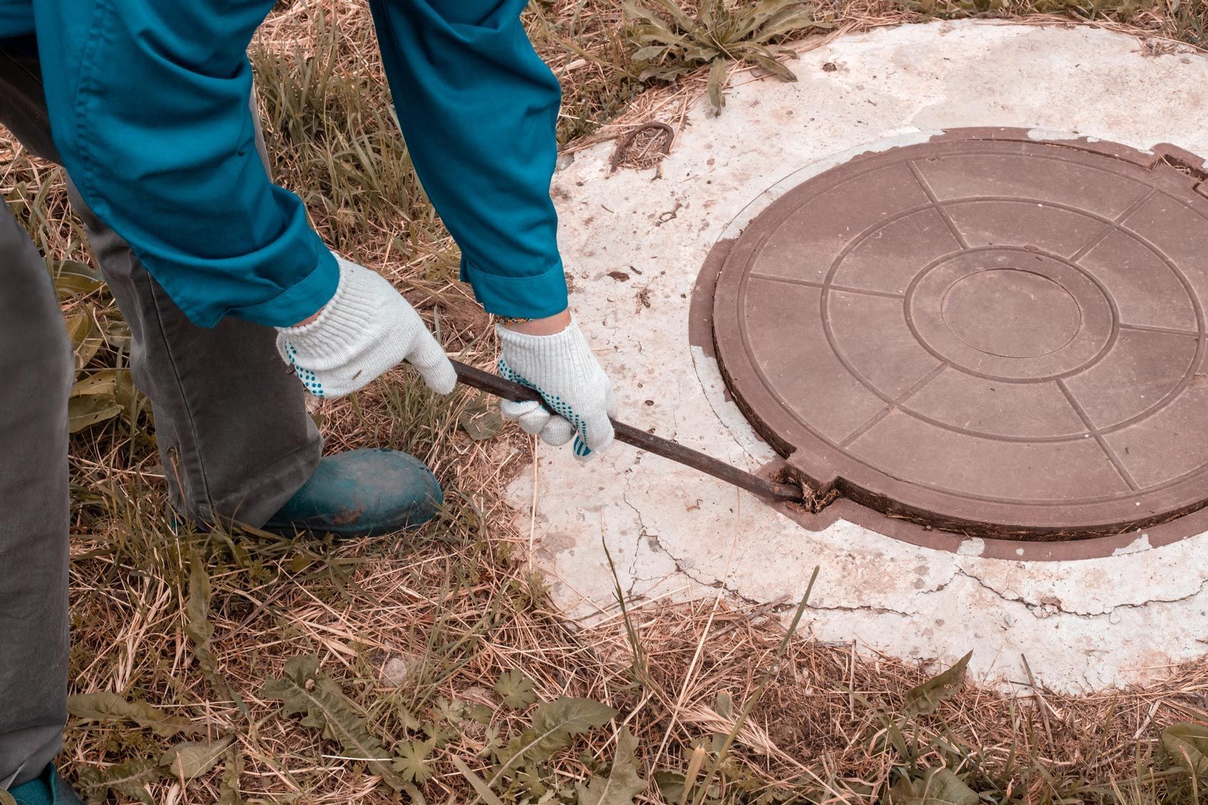A worker opens a septic tank hatch with a pry bar. A worker opens a septic tank hatch with a pry bar.