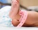 Baby’s foot with a pink hospital ID band resting on a bed