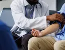 Doctor taking a seated patient’s blood pressure with a cuff in a clinic waiting area