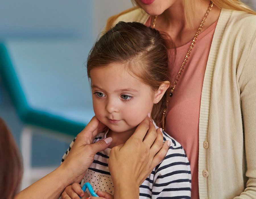 Child being comforted by an adult, with hands gently holding her shoulders in a bright indoor setting