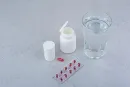 Medicine bottle, capsule, blister pack, and glass of water on a gray surface