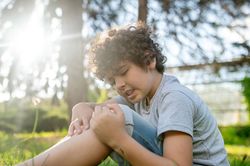 Person sitting on grass outdoors, holding a bent knee in bright sunlight.