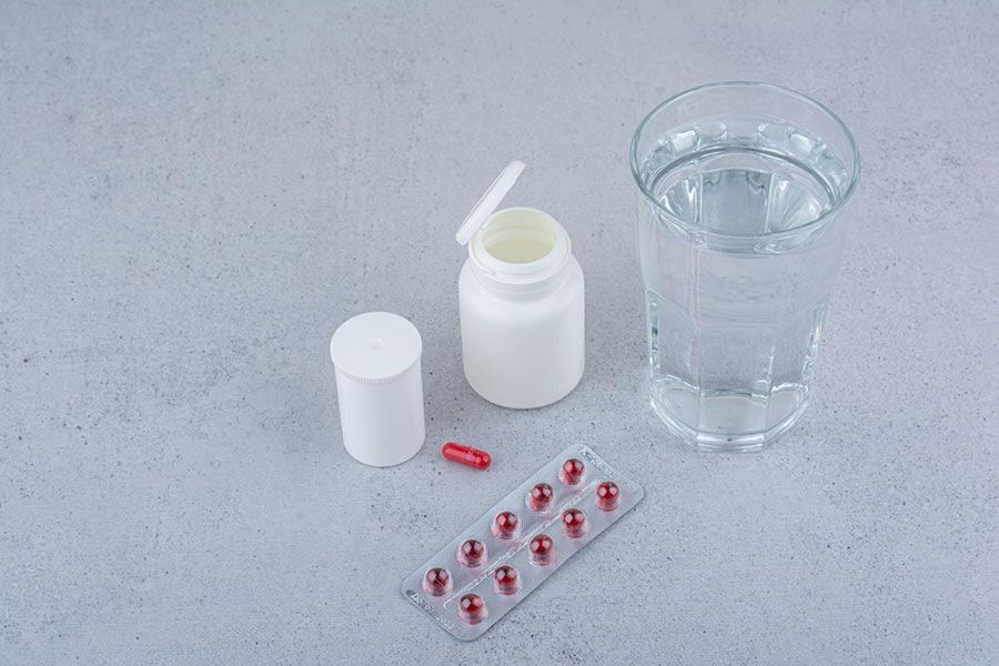 Medicine bottle, one pill, blister pack, and a glass of water on a table