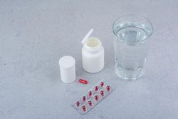 Medicine bottle, one pill, blister pack, and a glass of water on a table