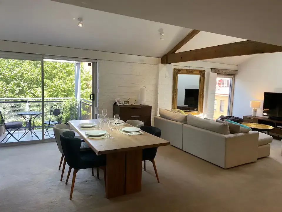 Boxwood IXL Open-concept living space: dining table, sofa, balcony, with natural light and visible wood beams.