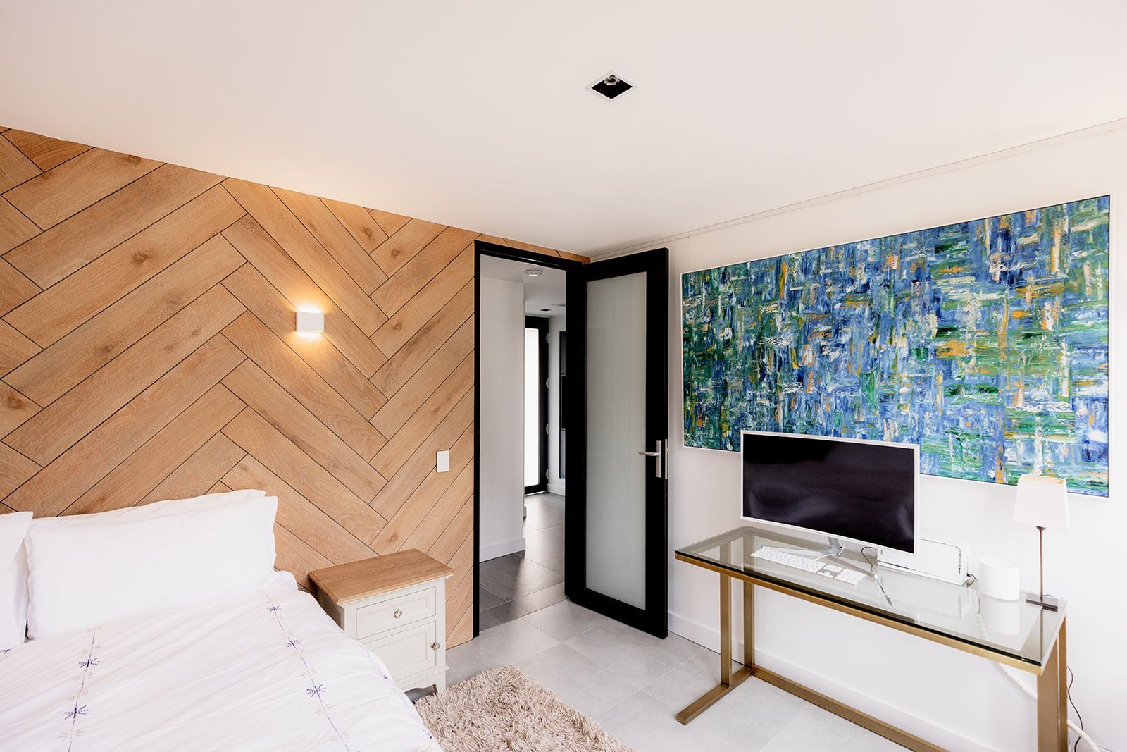 A bedroom with a bed , desk , television and painting on the wall.