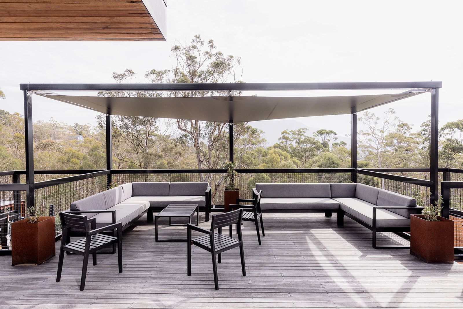 A wooden deck with a couch and chairs under a canopy.