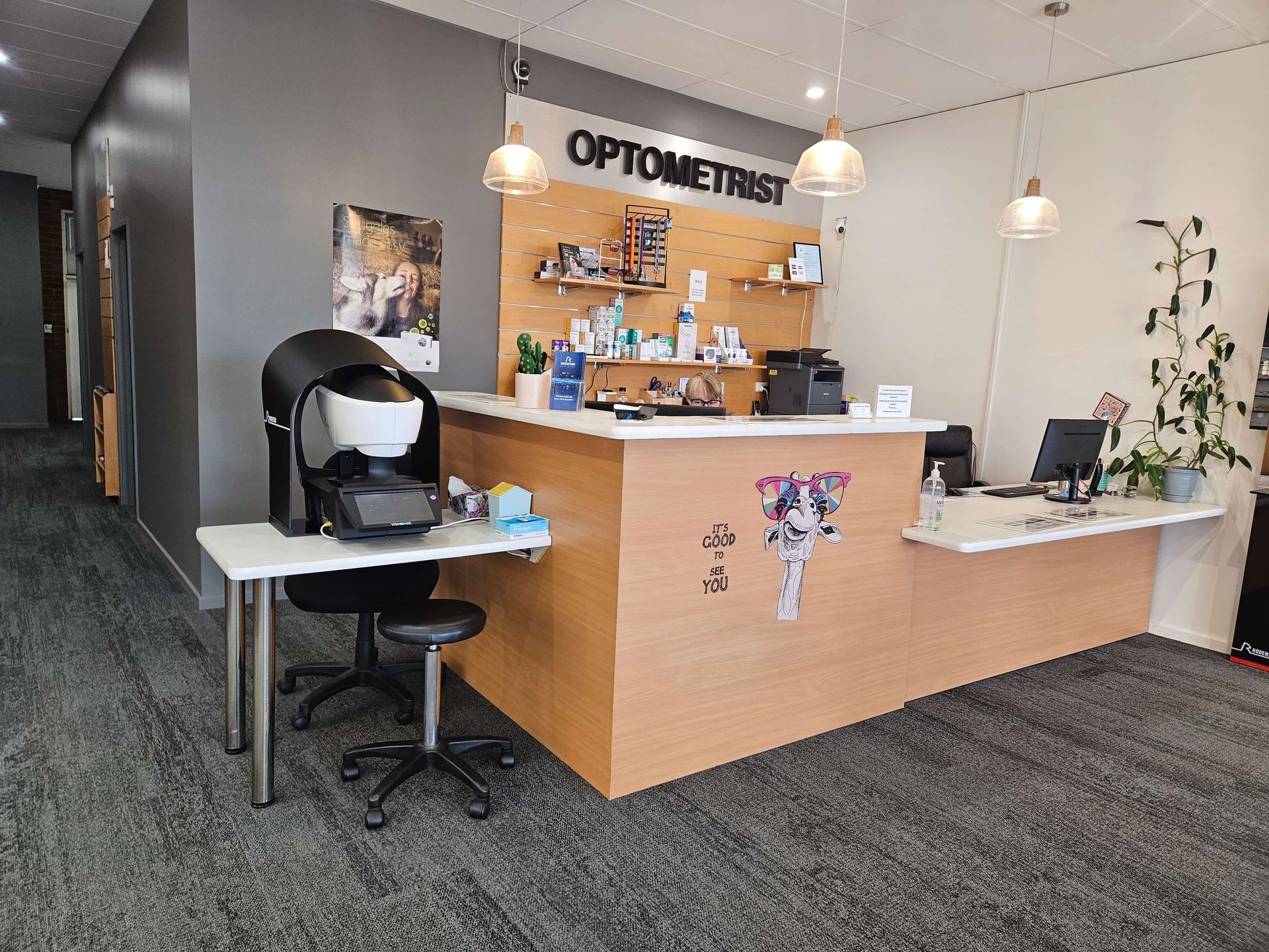 Interior view of an eye care center in Cranbourne with wooden counters, spherical light fixtures, and eyewear displays on the walls.