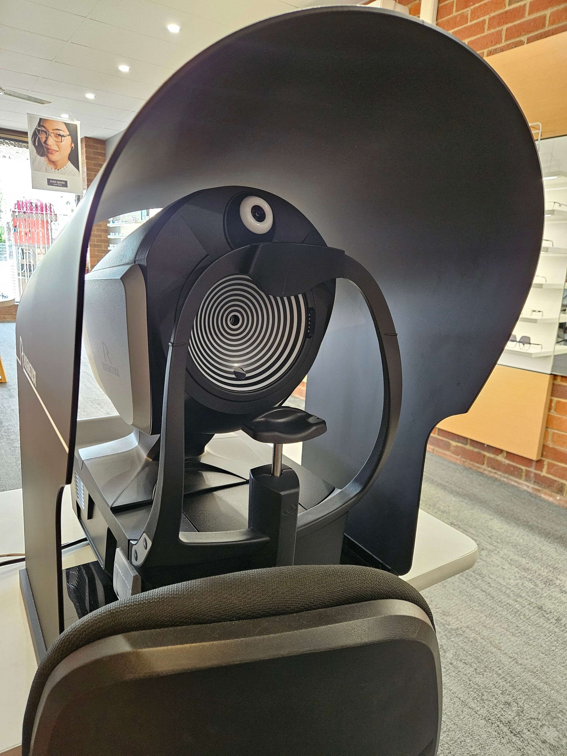 An eye exam room with a patient chair, phoropter, slit lamp, and multiple monitors displaying images of an eye.