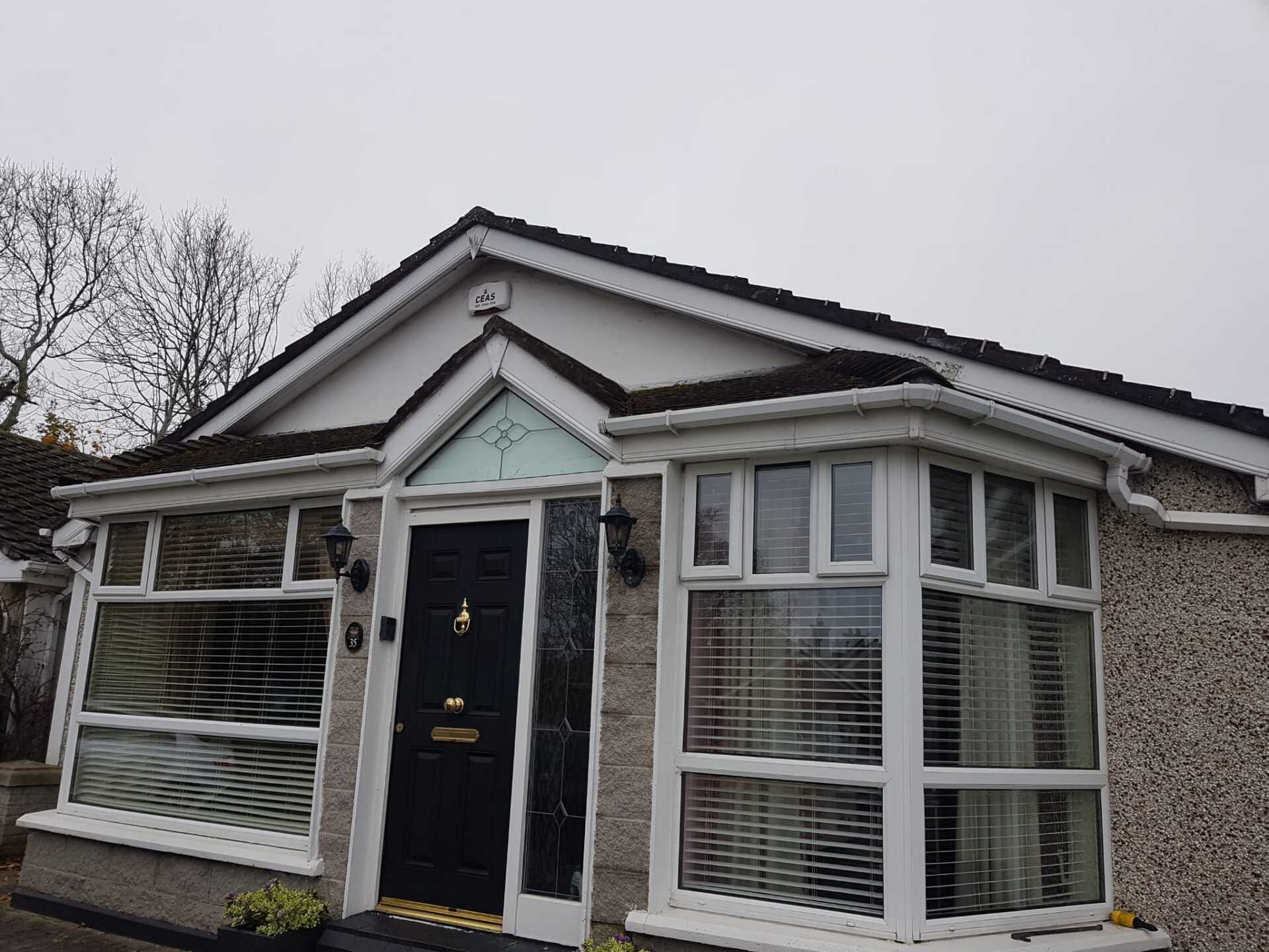A one-story house with a black door and bay window under a cloudy sky.