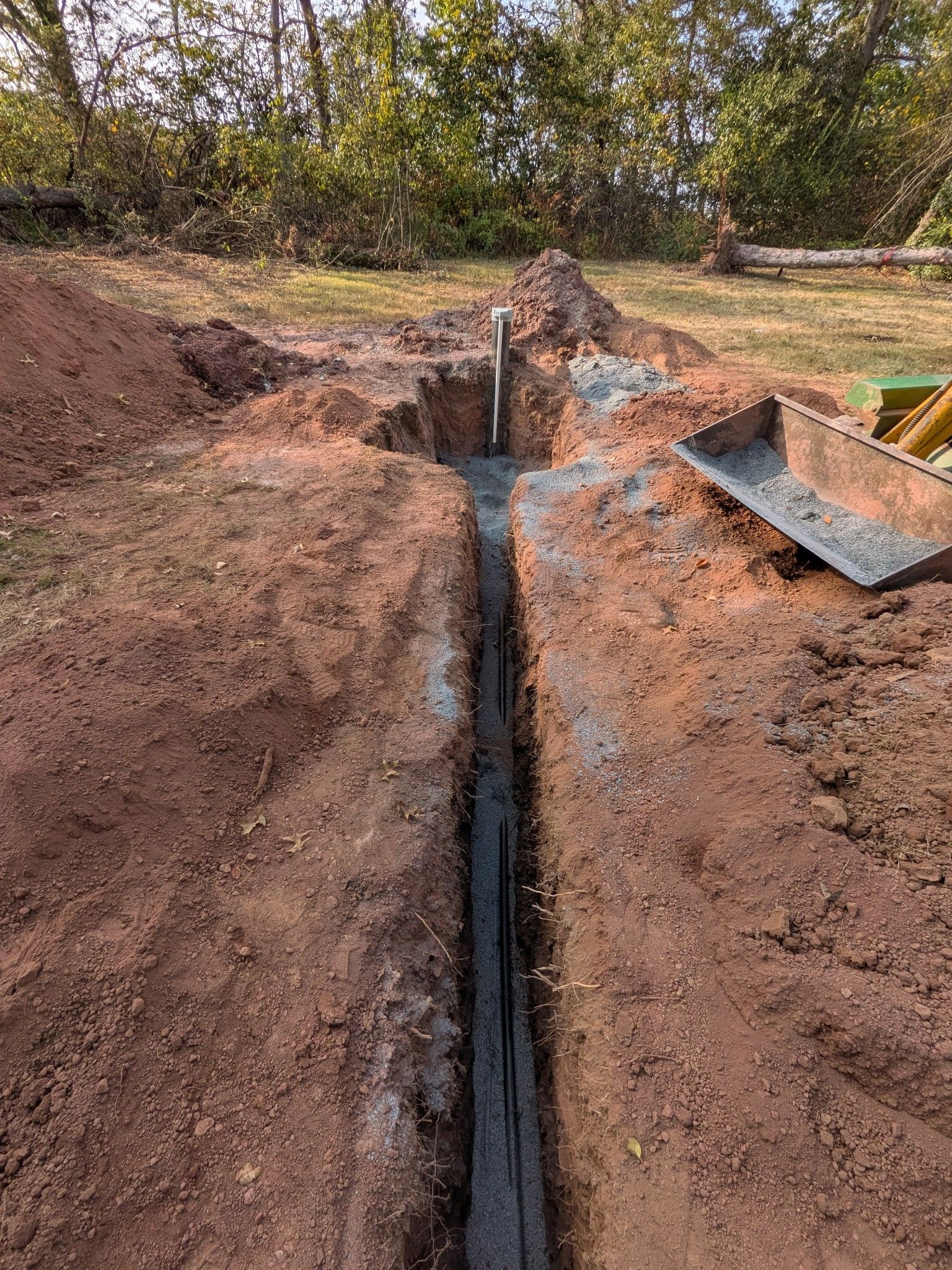 Freshly dug trench in a dirt construction site with a narrow channel and a metal plate on the right