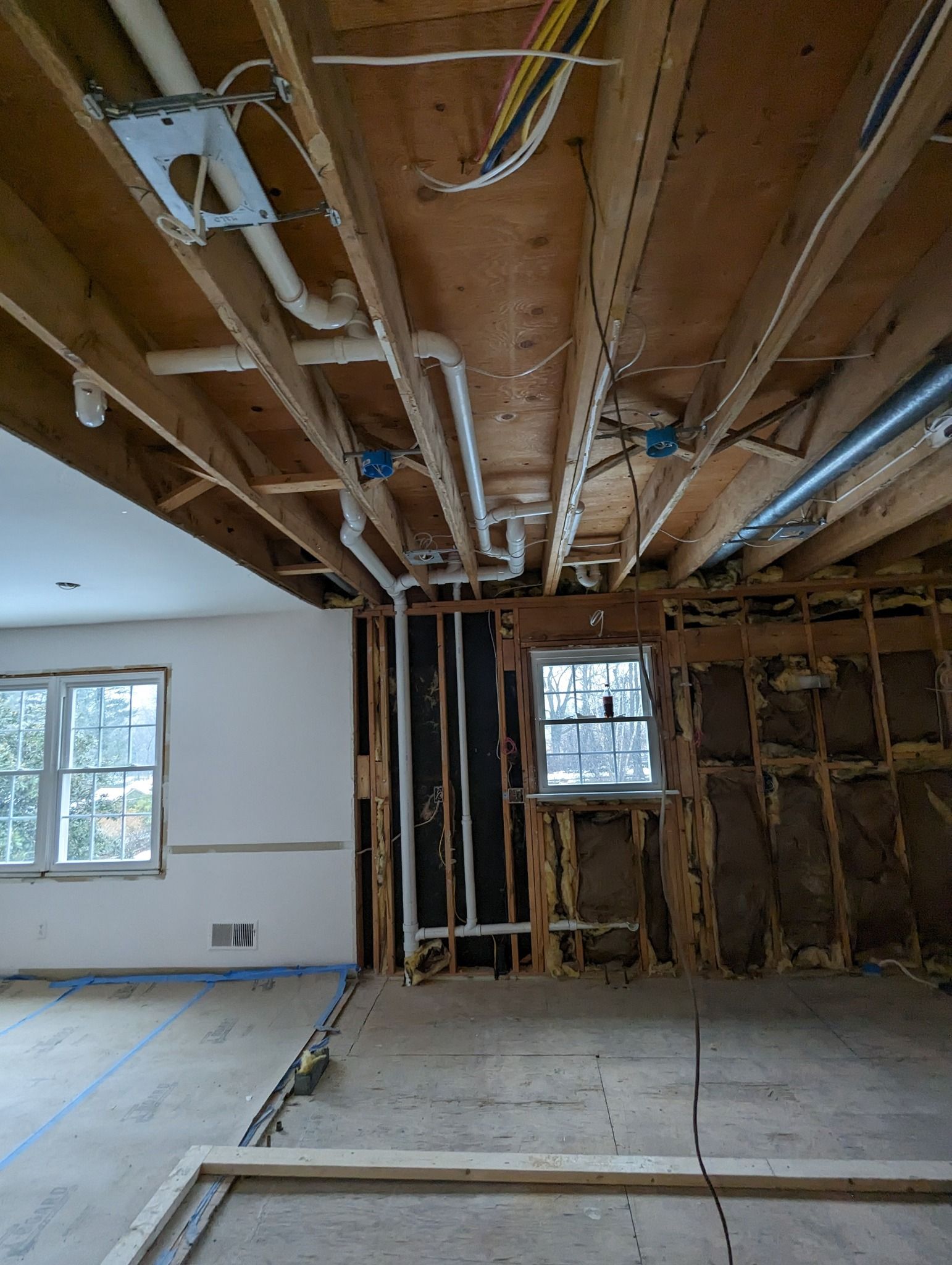 Interior renovation with exposed ceiling joists, wiring, and unfinished walls in a room with windows.