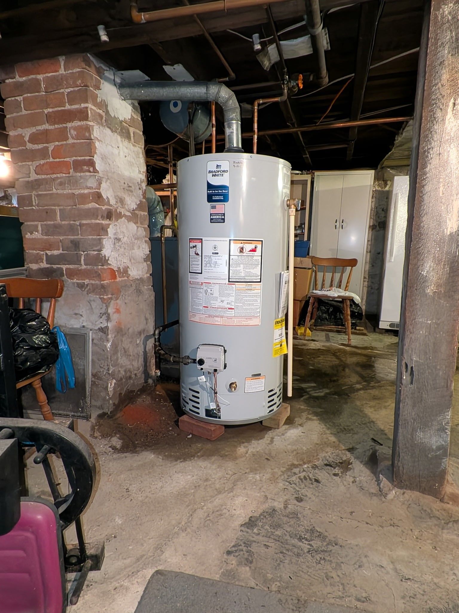 Basement utility room with a white water heater, exposed pipes, and a concrete floor.