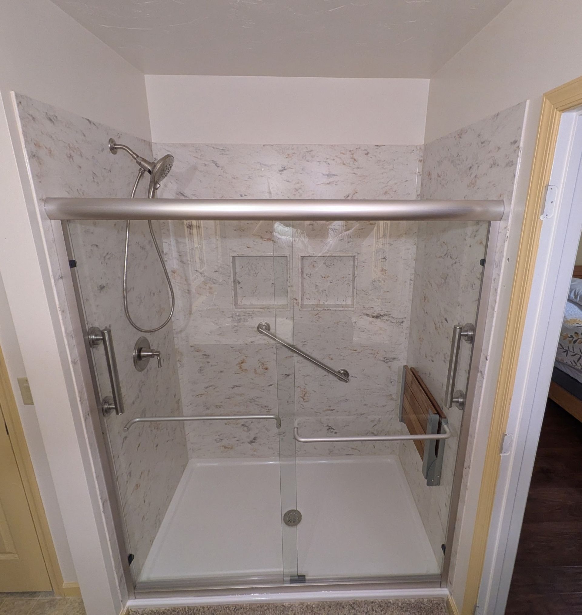 Glass walk-in shower with chrome grab bars, bench seat, and tiled walls in a bathroom