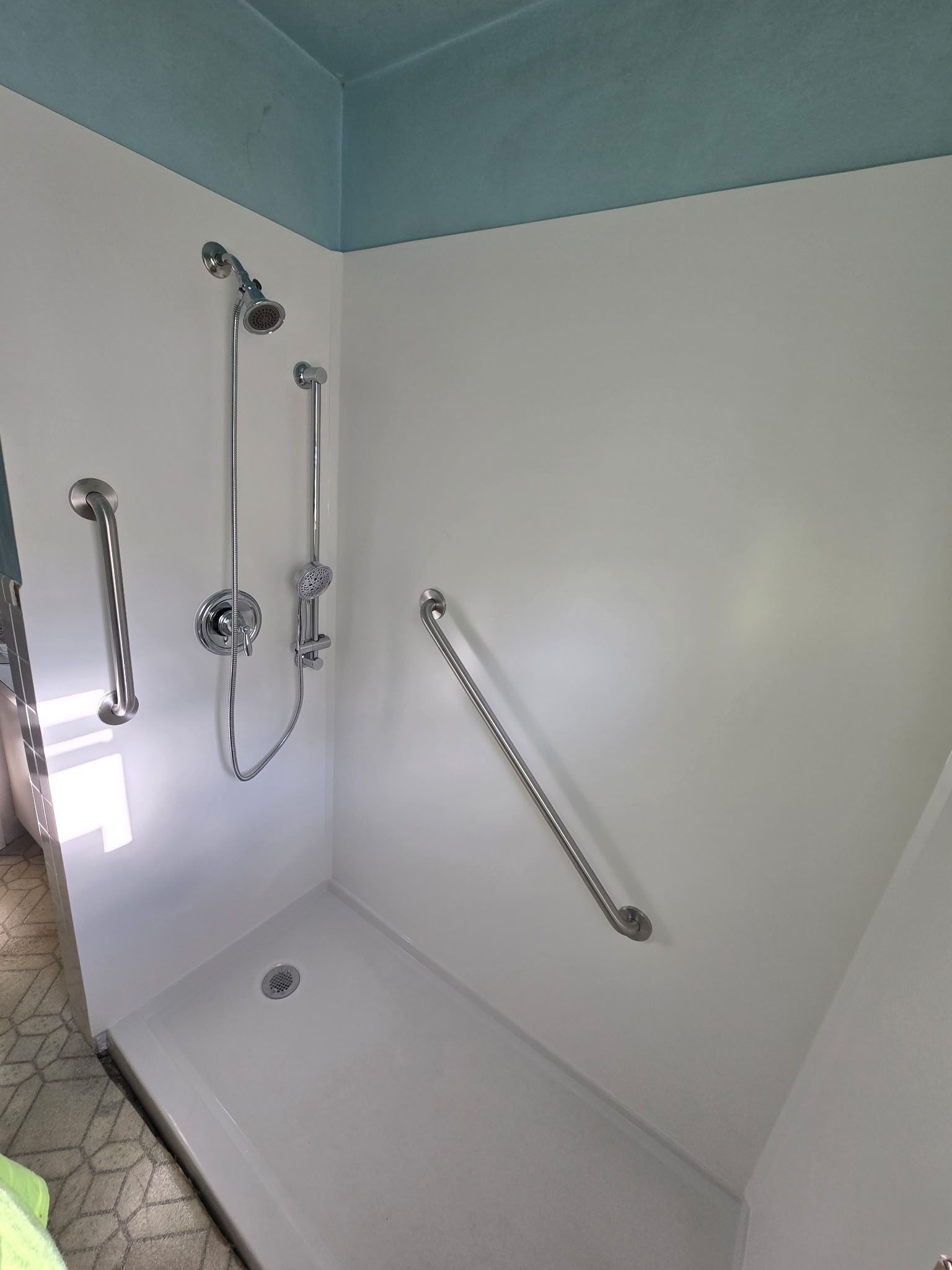 White accessible shower with grab bars, handheld showerhead, and a bench in a tiled bathroom.