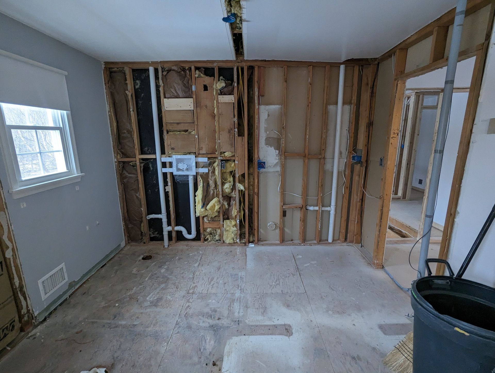 Partially demolished room with exposed wall studs, insulation, and a bucket on the floor