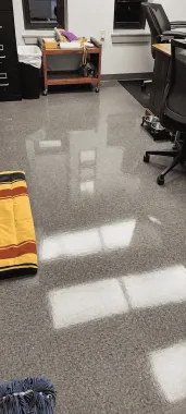 Office floor with reflective gray carpet, desks, chairs, and sunlight patches.
