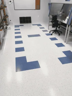 Lab room floor with blue tape markers, white worktables, a chair, and a wall vent.