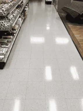 Empty store aisle with shiny white tile floor and shelves of packaged goods on the left.
