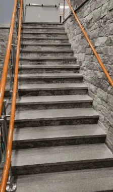 Steep concrete stairway with orange handrails between stone walls, leading upward to a landing