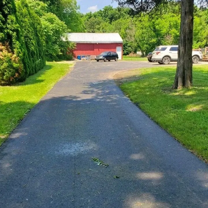A driveway leading to a red barn with cars parked on the side of it.