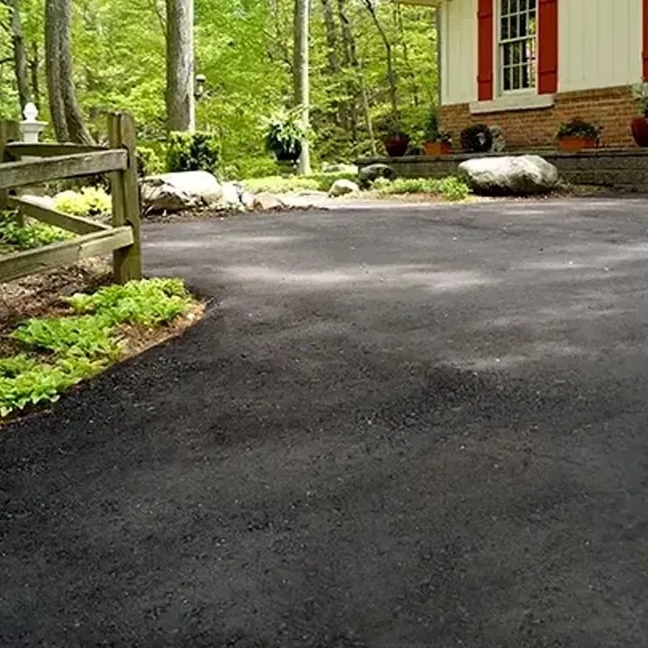 A driveway leading to a house with a wooden fence and trees in the background.