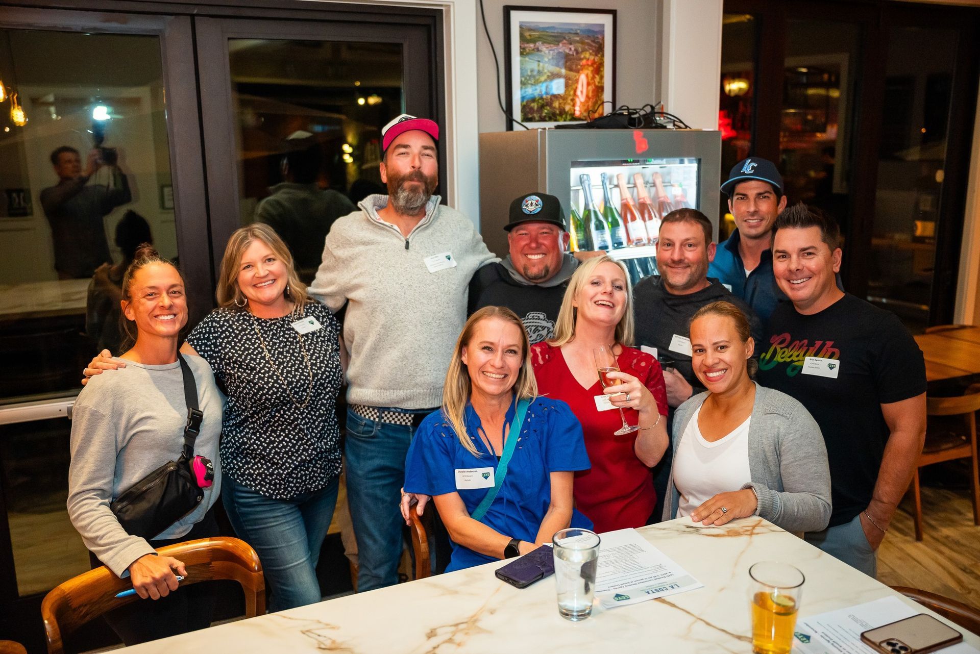 Group of people smiling around a table at an indoor gathering, at a volunteer appreciation event