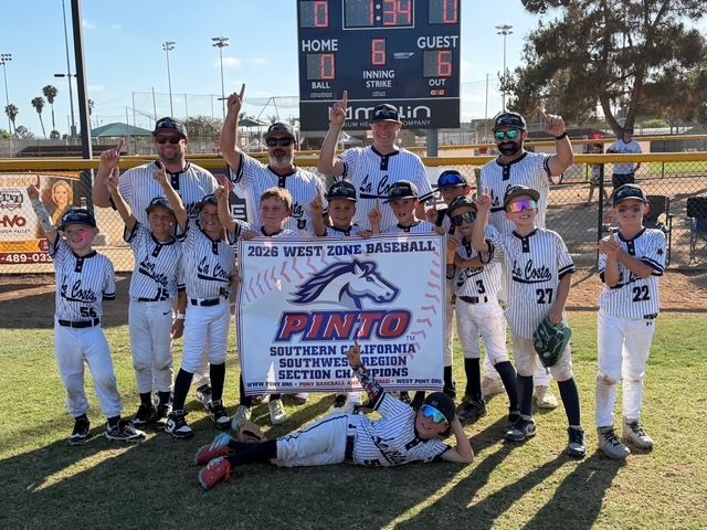 Youth baseball team posing on field with championship banner and trophy, celebrating at home plate.
