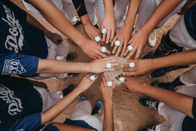 Hands gathered in a circle on a wooden floor, showing a team huddle with white-painted nails.
